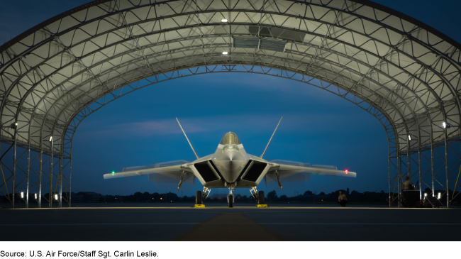 An Air Force F-22 Raptor in a lighted hangar at night.  